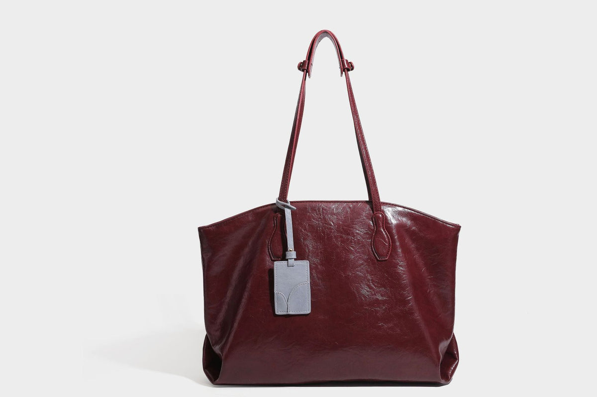 Übergroße, lässig fallende Tote-Bag aus glänzendem, geknittertem Lederimitat in dunklem Burgunderrot mit zwei langen Schulterriemen und kontrastierendem