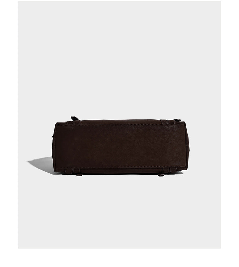 Weiche, zylinderförmige Schultertasche in Dunkelbraun mit silberfarbenen Riemen mit Ösen, Reißverschluss oben, seitlichen Schnallenbeschlägen und Quaste