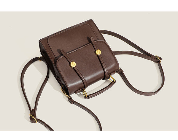 Structured mini satchel backpack with smooth leather-look finish, front flap pocket, gold-tone stud closures, and top handle