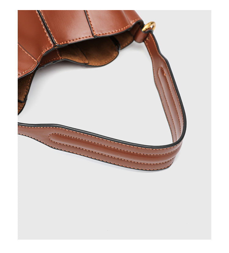 Smooth leather-look paneled bucket bag in brown with wide woven shoulder strap, gold-tone ring hardware, and detachable zip