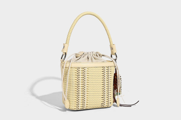 Small woven bucket bag with drawstring top, braided handle, detachable crossbody strap, and silver-tone ring hardware, detail