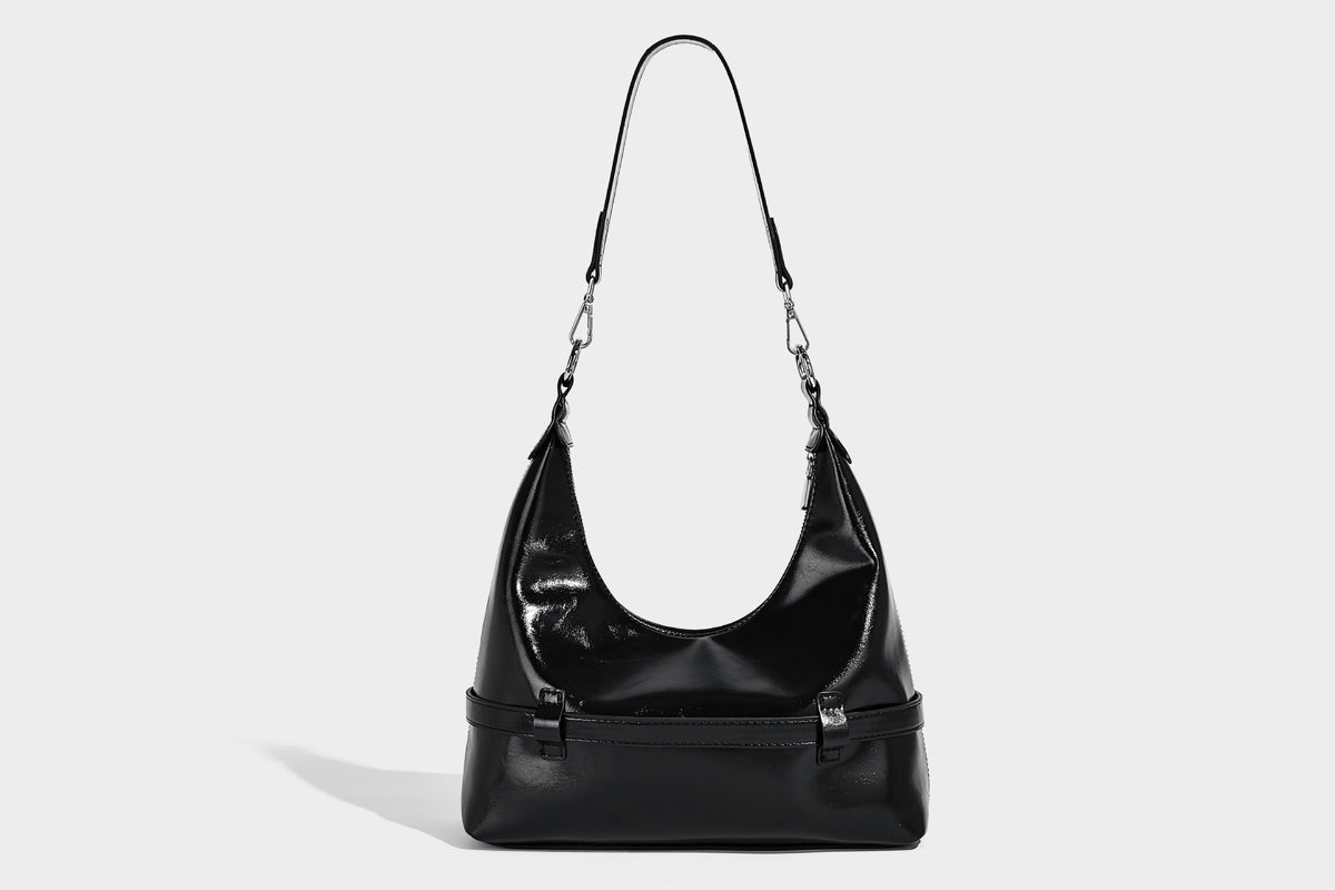 Glossy black slouchy hobo shoulder bag with silver-tone hardware, belt-style grommet strap at base, and long adjustable