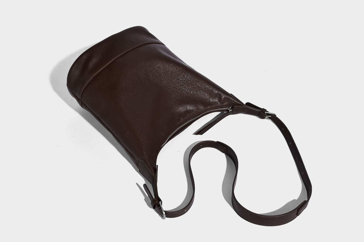 Slouchy bucket hobo shoulder bag in dark brown with glossy leather-look finish, top zip closure, and long adjustable, detail