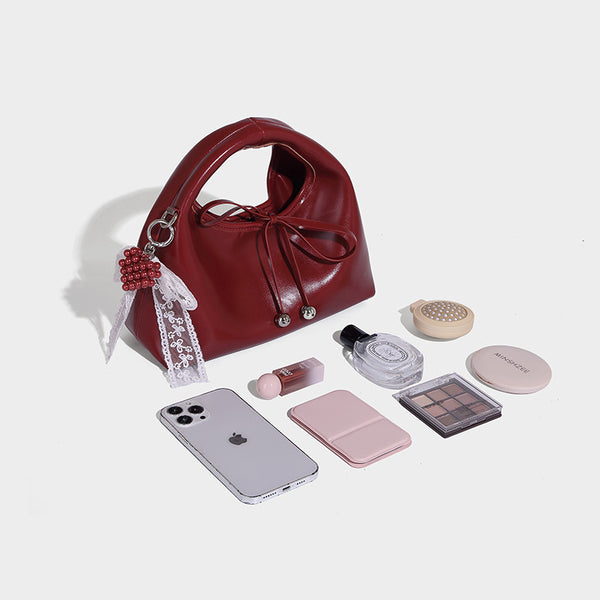Kleine glänzende kuppelförmige Henkeltasche in Lederoptik mit Zugbandverschluss, weißem Spitzen-Schleifenanhänger und silberfarbenen Beschlägen
