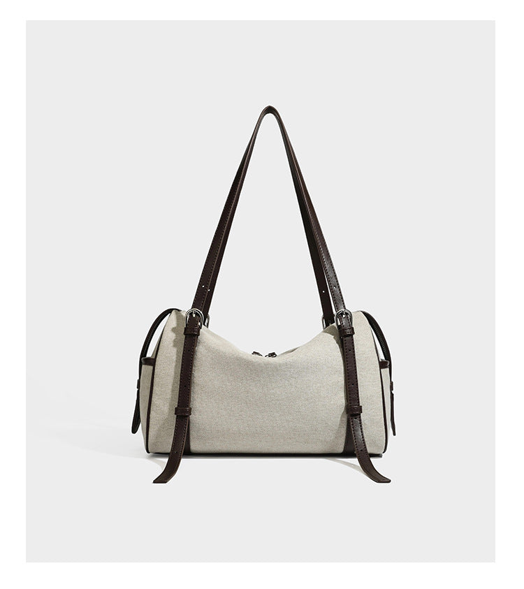 Beige canvas barrel bag with dark brown leather-look trim, silver-tone hardware, top zip closure, and adjustable shoulder