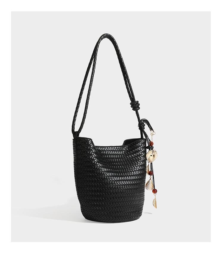 Olive green woven leather-look bucket bag with braided crossbody strap, knotted adjustment, and gold-tone tassel charm with