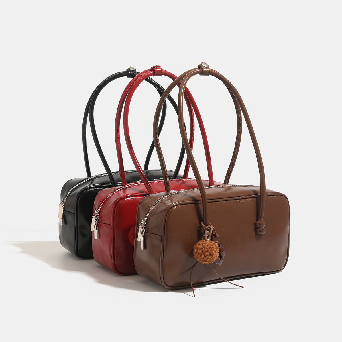 Boxy rectangular bowling shoulder bag with glossy leather-look finish, double rounded straps, top zip closure, and removable
