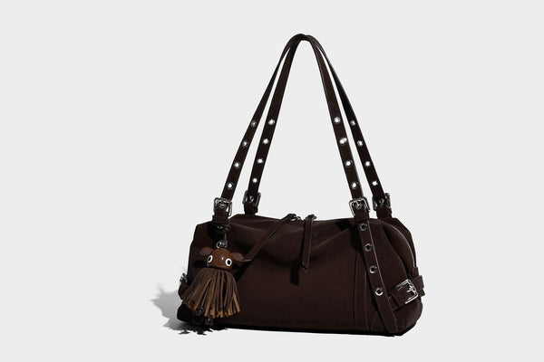 Weiche, zylinderförmige Schultertasche in Dunkelbraun mit silberfarbenen Riemen mit Ösen, Reißverschluss oben, seitlichen Schnallenbeschlägen und Quaste