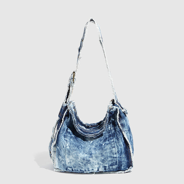 Slouchy distressed denim shoulder bag with frayed edges, white lace-up cross detail, front snap pocket, and long shoulder