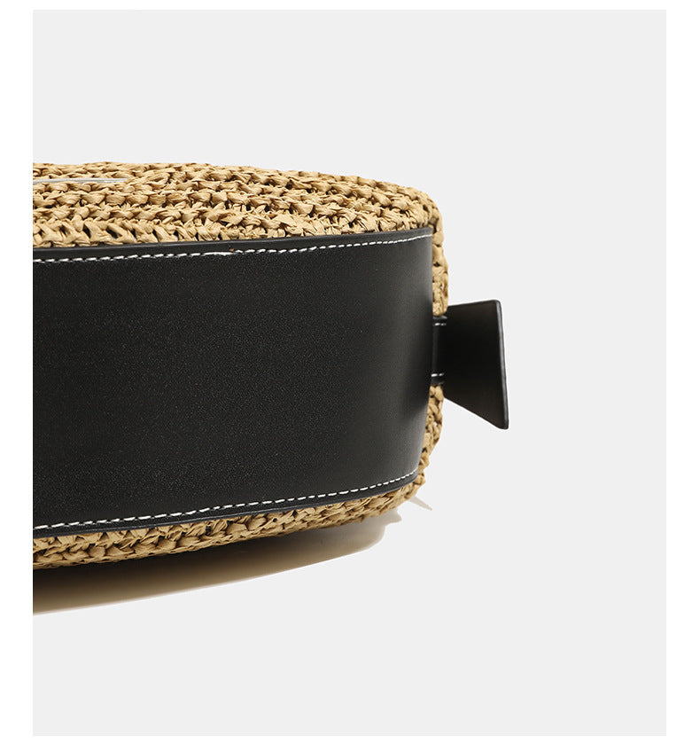 Compact crescent-shaped woven straw crossbody bag with black leather-look trim, top zip closure, and adjustable shoulder