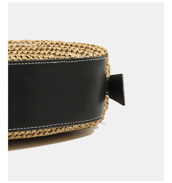 Compact crescent-shaped woven straw crossbody bag with black leather-look trim, top zip closure, and adjustable shoulder
