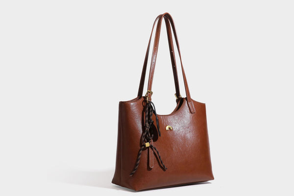 Structured smooth leather-look tote bag with long shoulder strap, gold-tone hardware, and hanging tassel-coin charm, detail