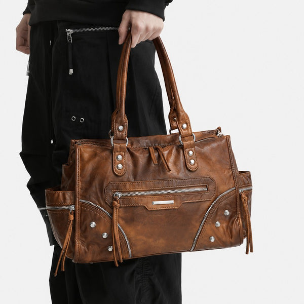 Large distressed leather-look moto tote bag with silver rivets, tassel zip pulls, front zip pocket, and dual top handles