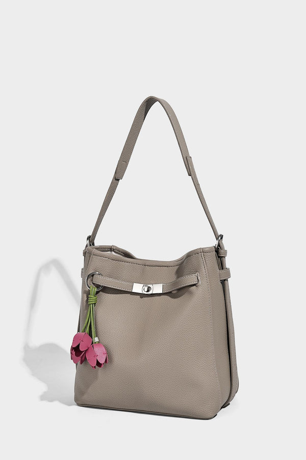 Soft-structured pebbled bucket shoulder bag with front turn-lock strap detail, adjustable strap, and hanging floral tassel