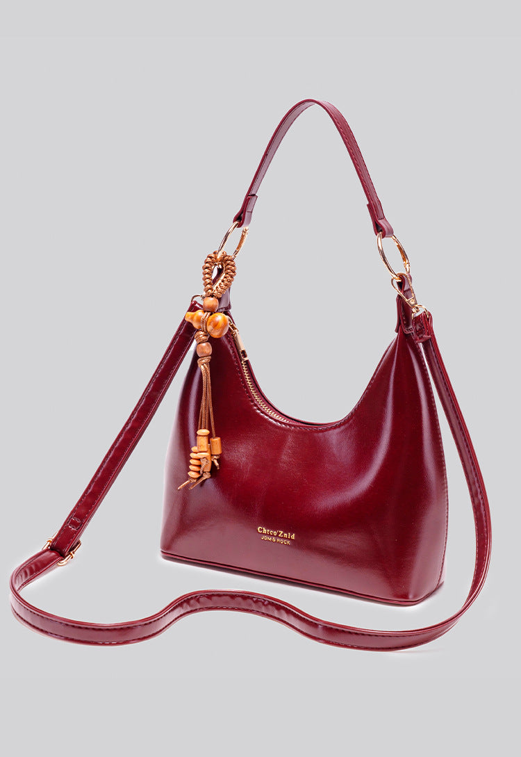 Glossy crescent hobo shoulder bag in deep burgundy with beaded wood tassel charm and gold-tone ring hardware, detail view 12