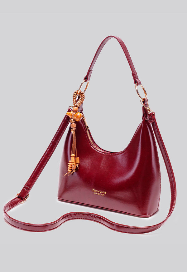 Glossy crescent hobo shoulder bag in deep burgundy with beaded wood tassel charm and gold-tone ring hardware, detail view 12