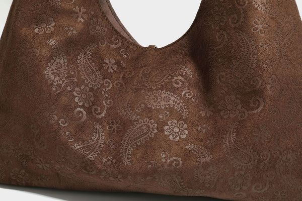 Slouchy boho hobo shoulder bag in embossed brown suede-look finish with beaded strap, cord tassels, and brass-tone leaf