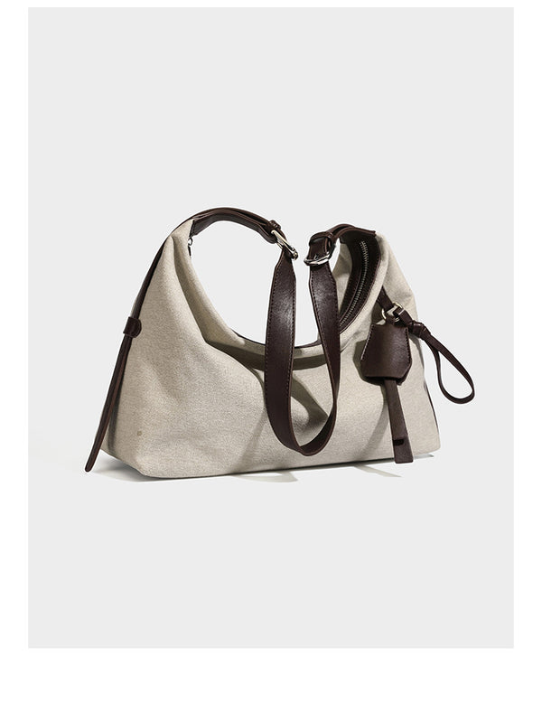 Lässig geschnittene Hobo-Schultertasche aus Canvas in Haferflockenfarbe mit dunkelbraunem Besatz in Lederoptik, silberfarbenem Reißverschluss und langem, verstellbarem