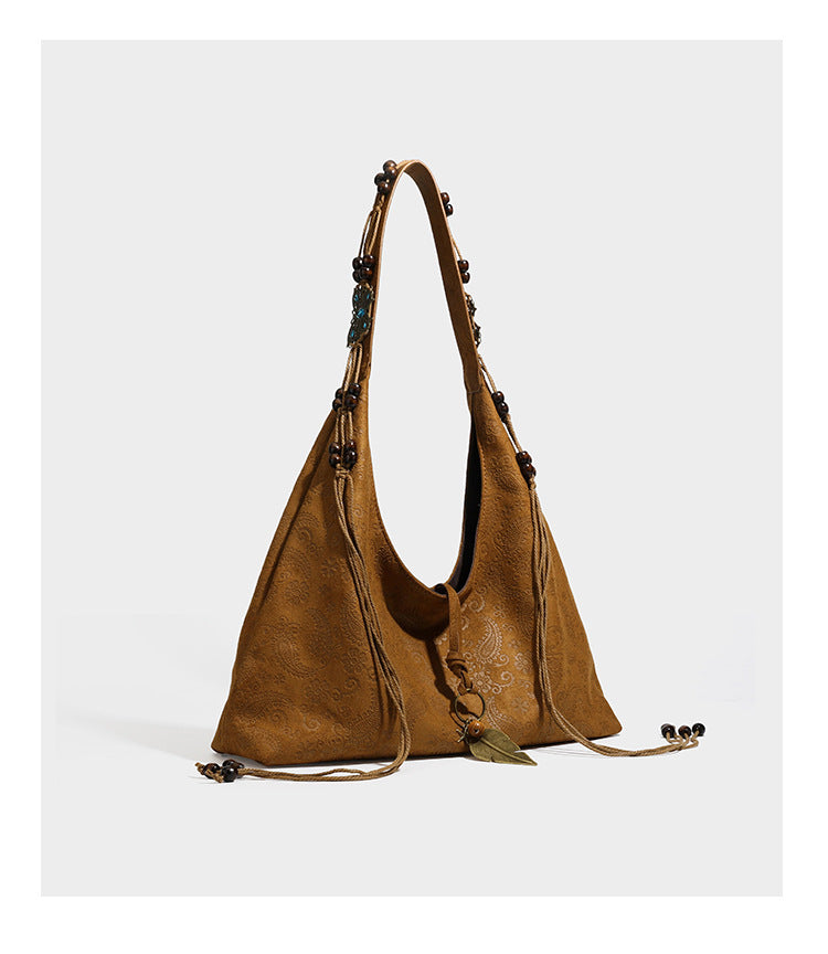 Slouchy boho hobo shoulder bag in embossed brown suede-look finish with beaded strap, cord tassels, and brass-tone leaf