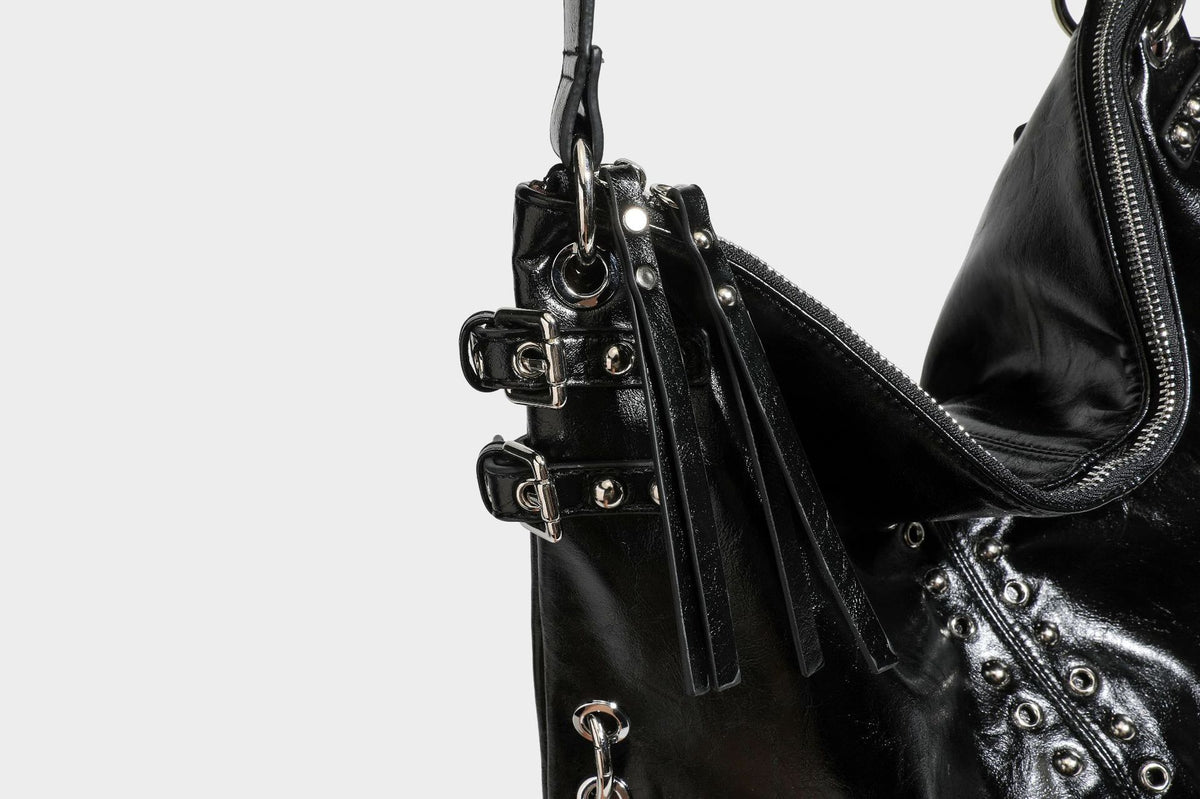 Black glossy leather-look slouchy shoulder bag with silver stud and eyelet hardware, top zip closure, front zip pocket, and