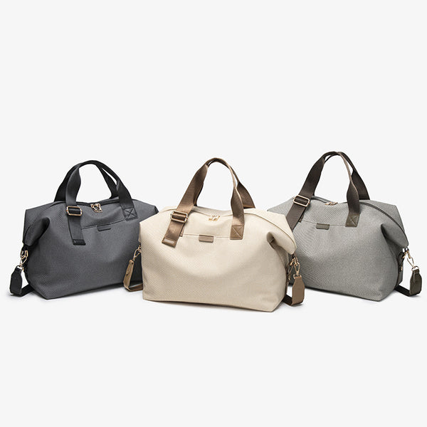 Structured woven duffel bag with dual tan webbing handles, detachable shoulder strap, top zip closure, and gold-tone