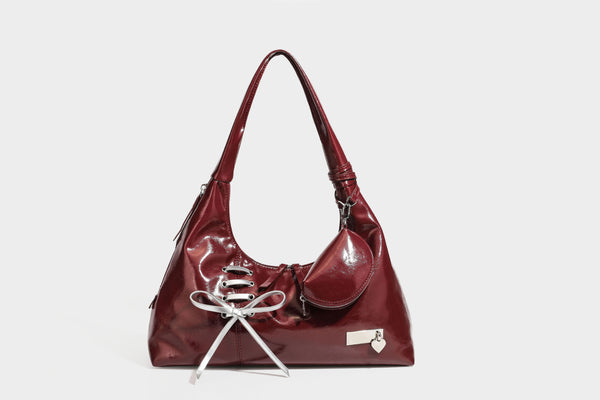Weich fallende Hobo-Schultertasche in glänzender Lederoptik mit silberfarbenen Ösen zum Schnüren und Schleifenband auf der Vorderseite, Detailansicht