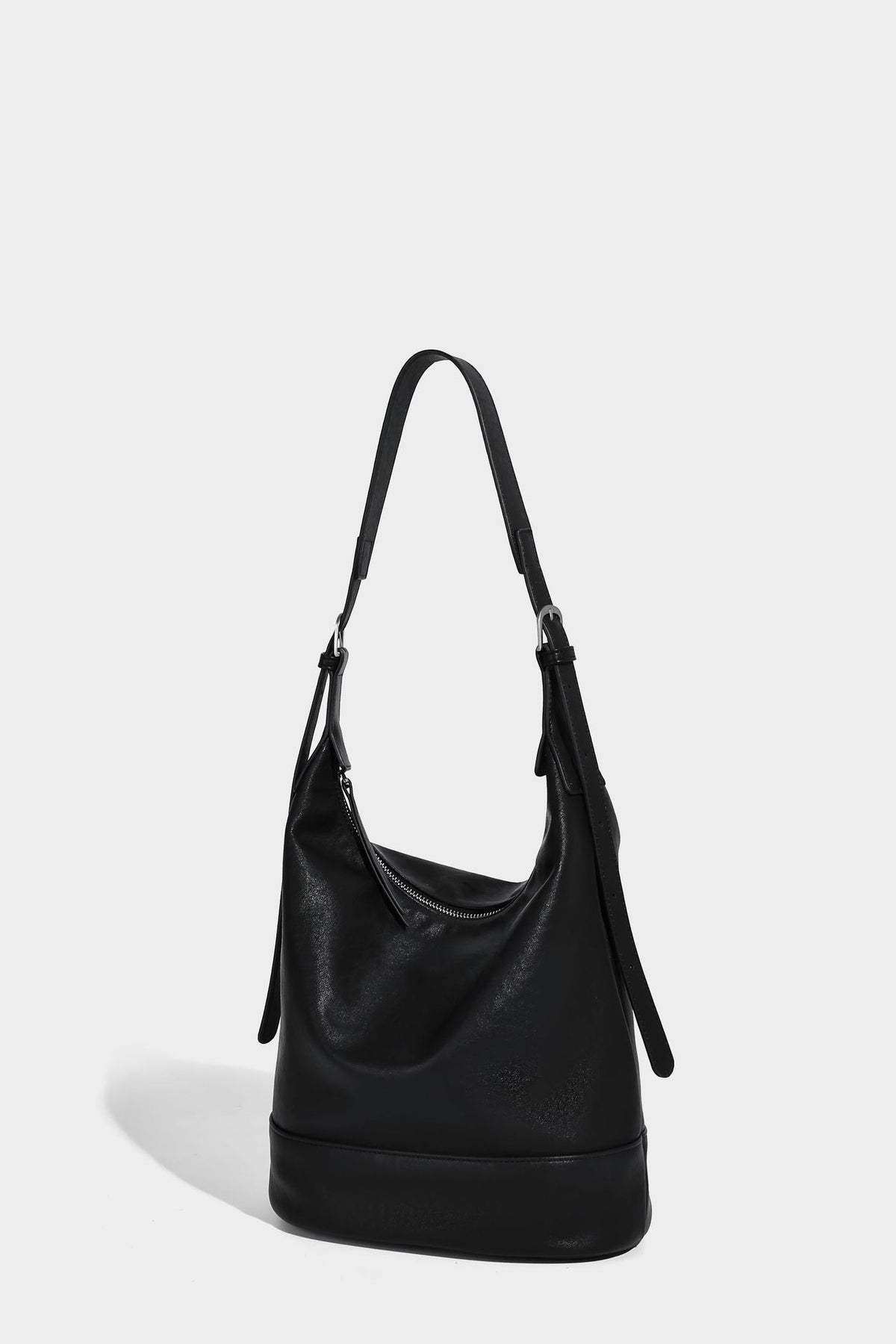 Slouchy bucket hobo shoulder bag in dark brown with glossy leather-look finish, top zip closure, and long adjustable, detail