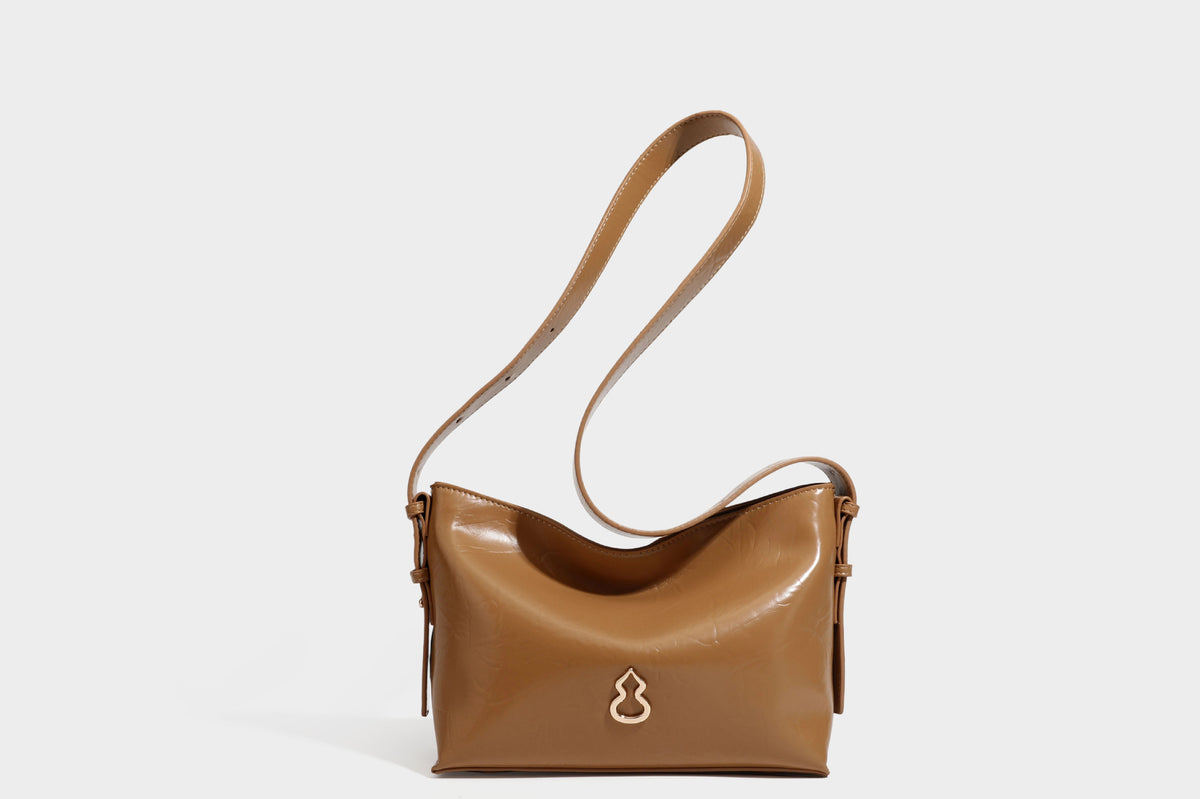 Lässig fallende Hobo-Schultertasche mit offenem Oberteil aus glänzender, karamellbrauner Lederoptik, mit Logo-Beschlägen in Goldoptik und langem, verstellbarem
