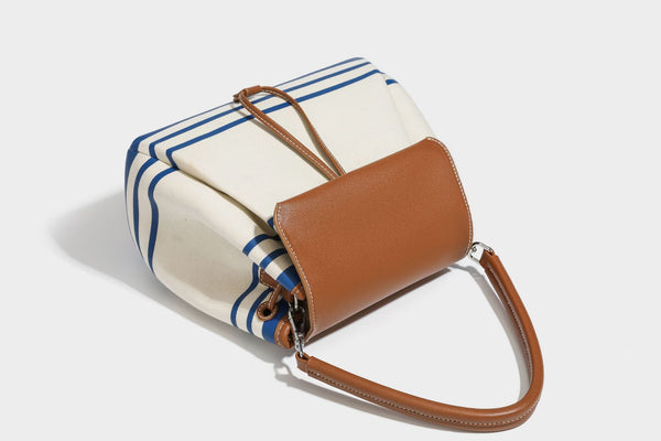 Cream canvas bucket bag with blue horizontal stripes, tan leather-look flap and trim, drawstring closure, silver-tone, detail