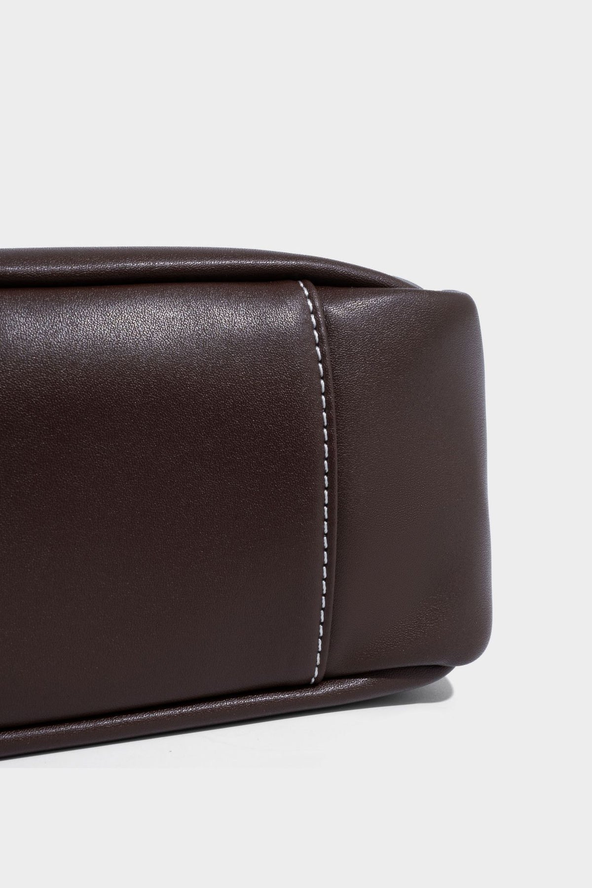 Structured dark brown leather-look bucket bag with white contrast stitching, front wraparound belt buckle strap, and long