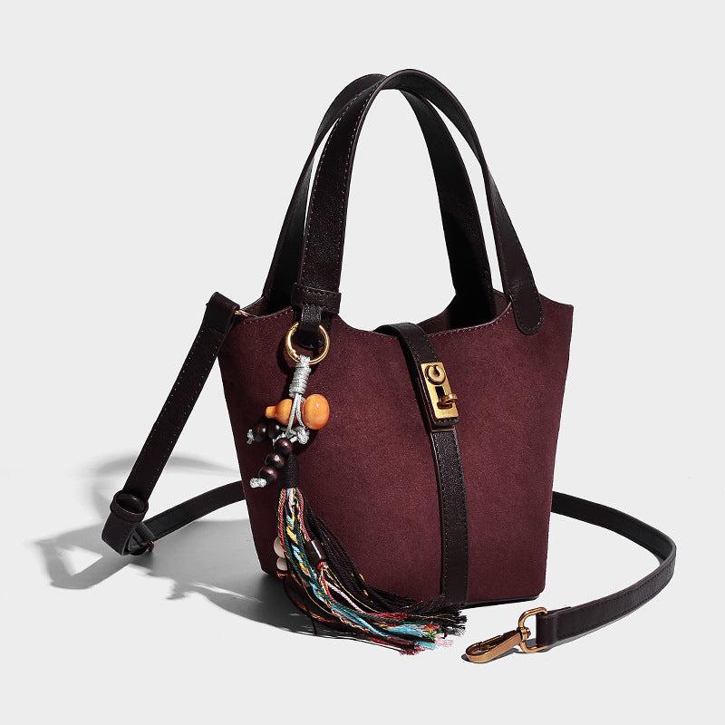 Small structured trapezoid tote bag in matte suede-look finish with black contrast trim, gold-tone front clasp, tassel charm
