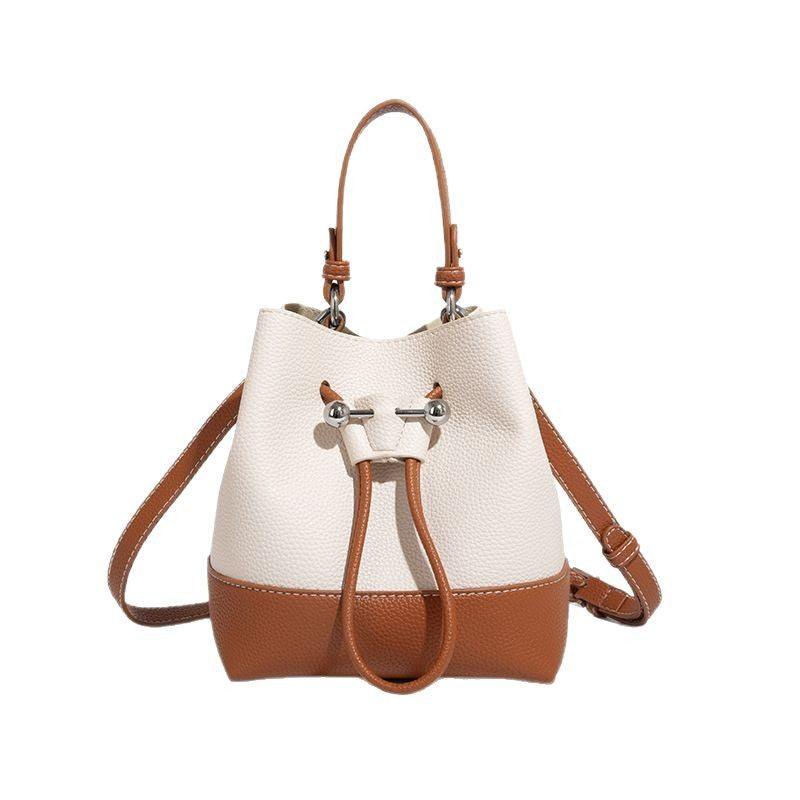 Small two-tone pebbled drawstring bucket bag with tan contrast base, metal toggle hardware, short top handle, and detachable