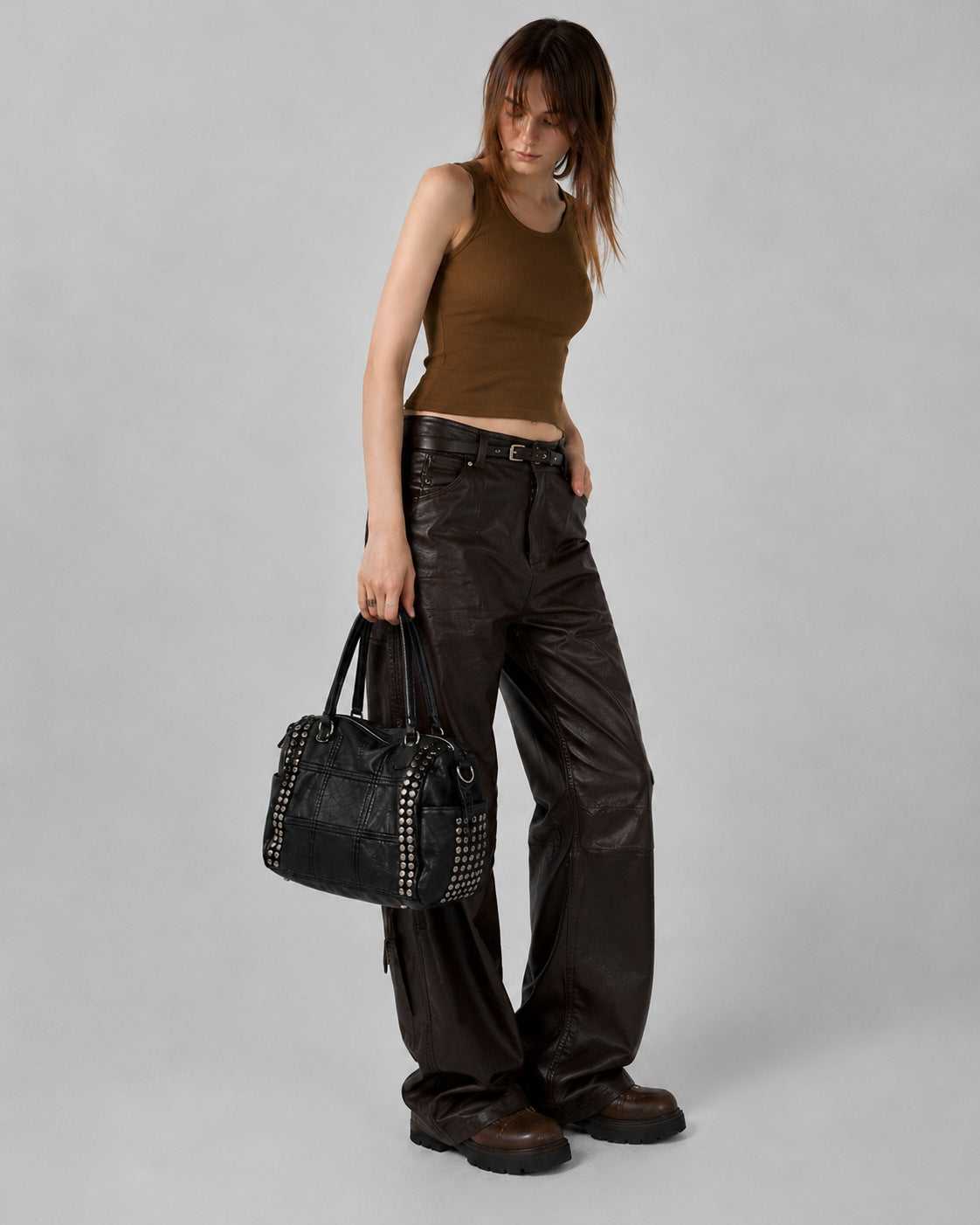 Black leather-look satchel bag with gunmetal rivet trim, grid-stitched paneling, dual rolled top handles, and curved zip