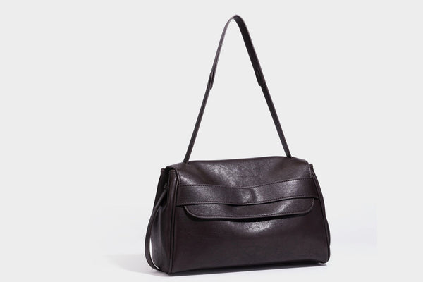 Strukturierte rechteckige dunkelbraune Schultertasche in Lederoptik mit Klappe, mehrlagigem Detail auf der Vorderseite und langem verstellbarem Riemen, Detailansicht