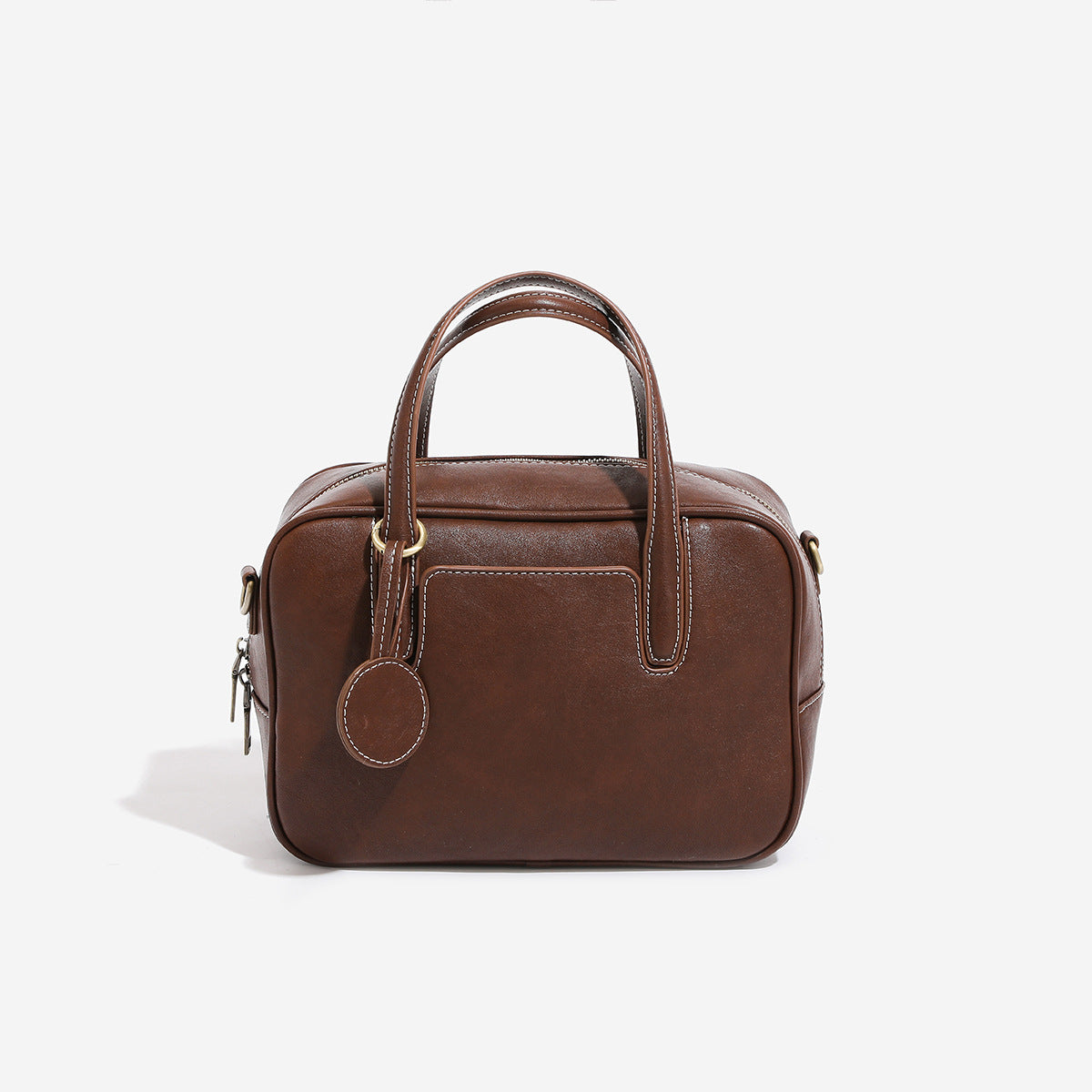 Structured boxy bowling-style tote bag in deep brown leather-look finish with dual top handles, front slip pocket, round