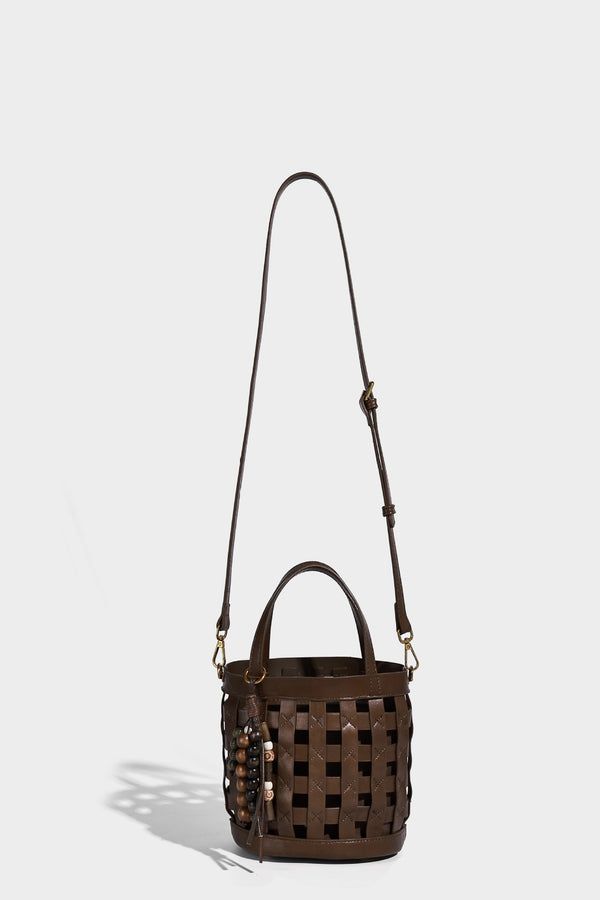 Small woven lattice bucket bag in brown leather-look finish with beaded tassel charm, dual top handles, and detachable