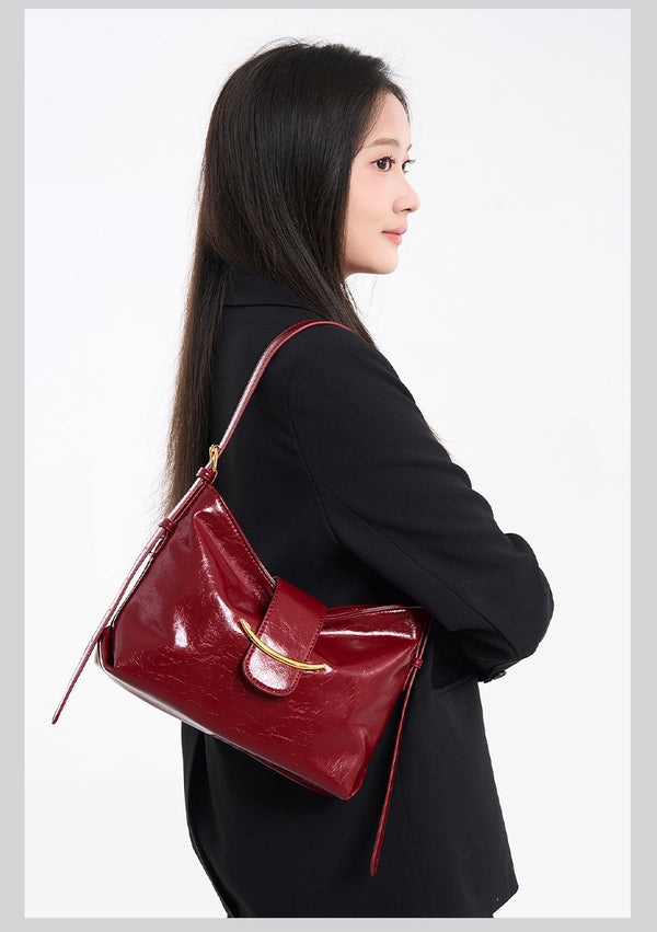 Glossy burgundy leather-look shoulder bag with curved gold-tone bar front closure, crinkled oil-wax texture, and adjustable