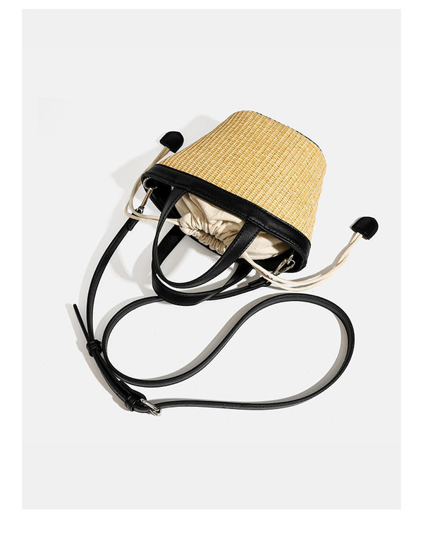 Kleine geflochtene Bucket Bag aus Stroh mit schwarzem Besatz in Lederoptik, zwei oberen Tragegriffen, cremefarbenem Futter mit Kordelzug und seitlichen Kordelverschlüssen