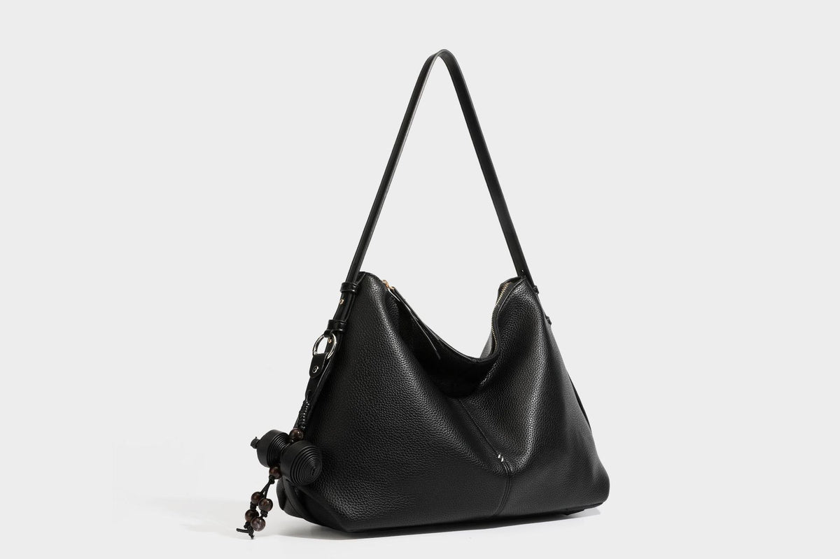 Slouchy hobo shoulder bag with pebbled leather-look finish, zip-top closure, gold-tone hardware, and hanging bead charm