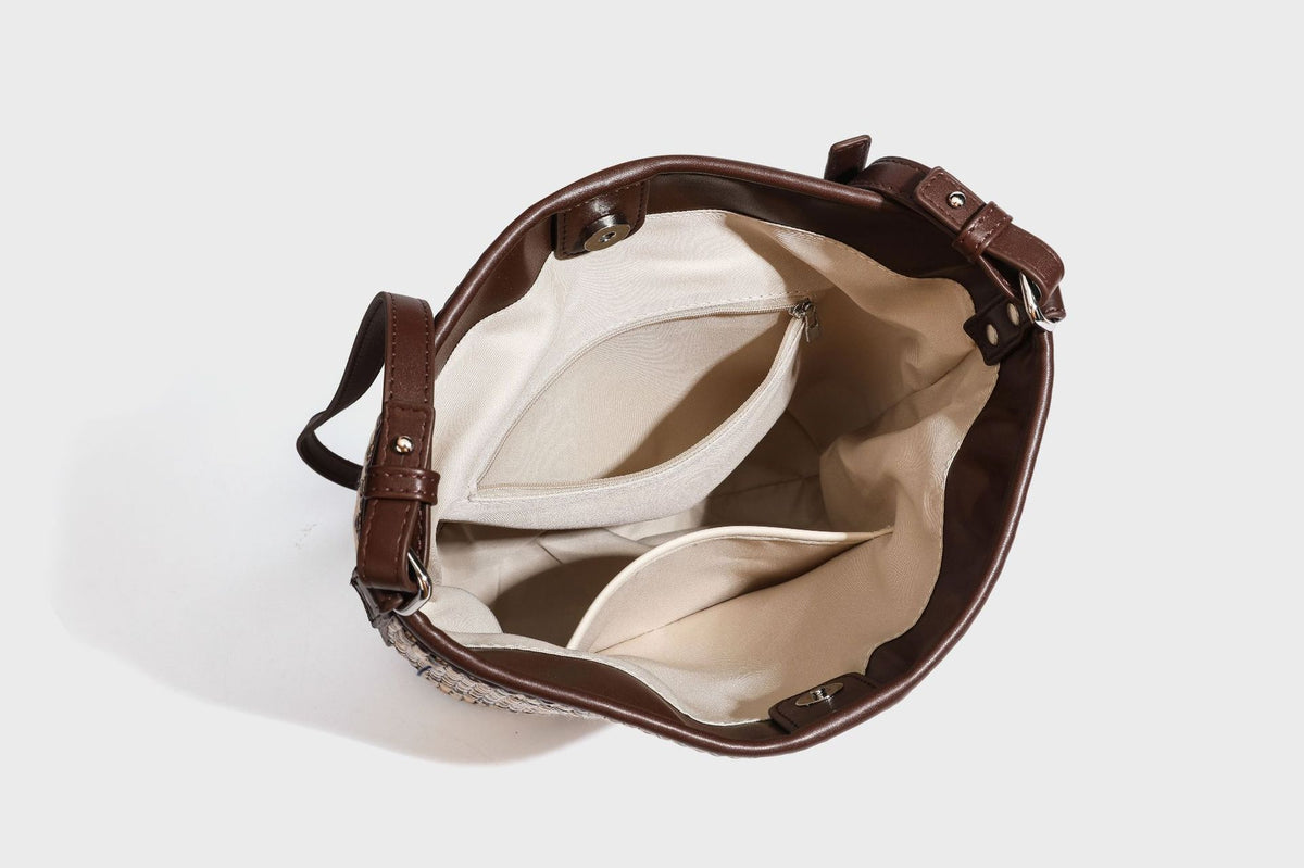 Woven stripe bucket shoulder bag in cream and dark brown with leather-look trim, knotted adjustable strap, and small shield