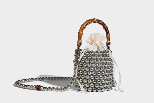 Small cylindrical bucket bag with glossy faux-pearl bead exterior, bamboo arched top handle, satin drawstring closure, and