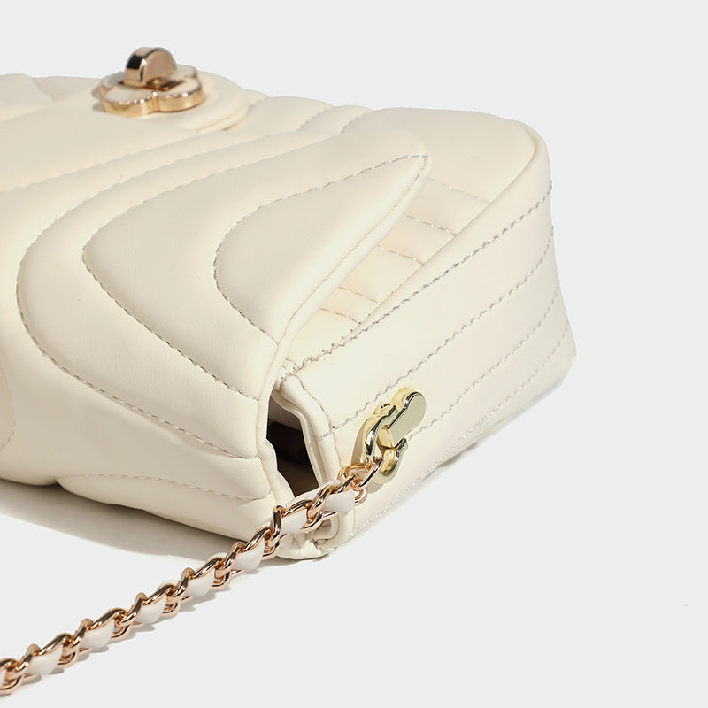 Compact cream quilted flap crossbody bag with wave stitching, gold-tone chain strap, and four-petal turn-lock clasp, detail