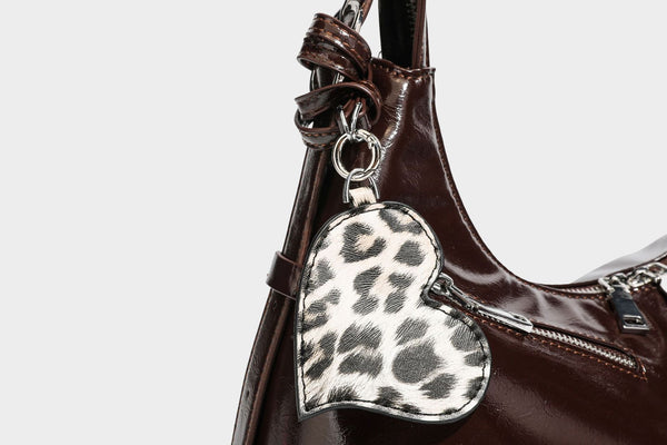 Glossy dark brown hobo shoulder bag with slim strap, front zip pocket, stud detail, and detachable leopard-print heart charm