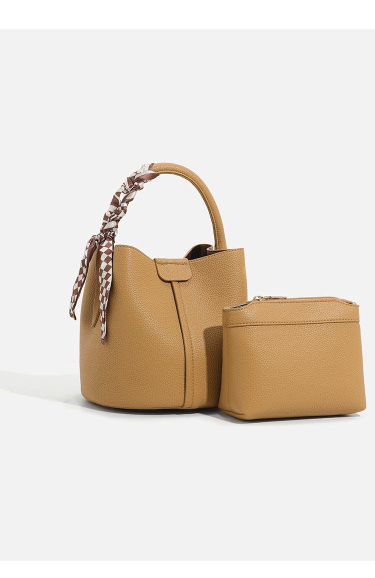 Pebbled leather-look bucket bag with checkered scarf-wrapped top handle, flap tab closure, gold-tone hardware, and matching