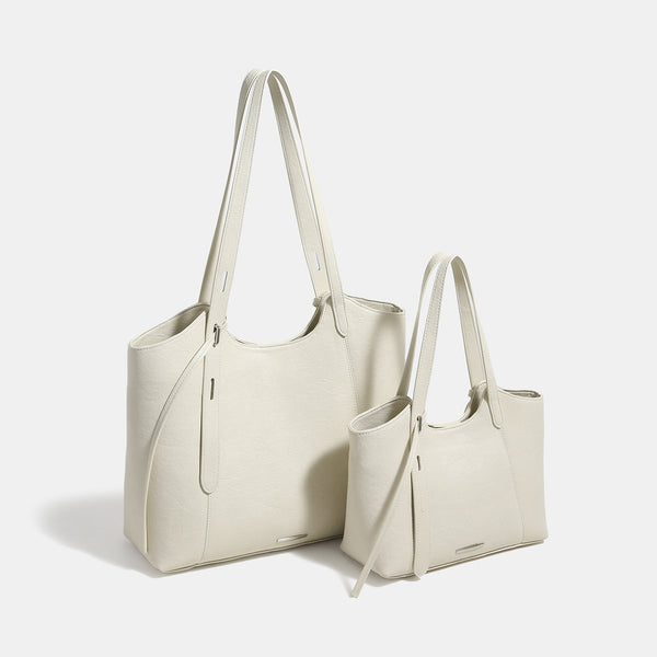 Structured trapezoidal tote bag with smooth leather-look finish, long black contrast shoulder straps, and dangling strap