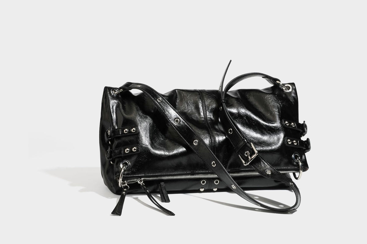 Black glossy leather-look slouchy shoulder bag with silver stud and eyelet hardware, top zip closure, front zip pocket, and