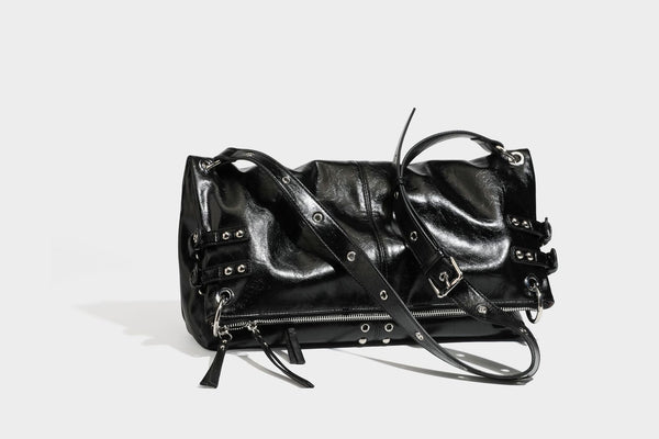 Black glossy leather-look slouchy shoulder bag with silver stud and eyelet hardware, top zip closure, front zip pocket, and
