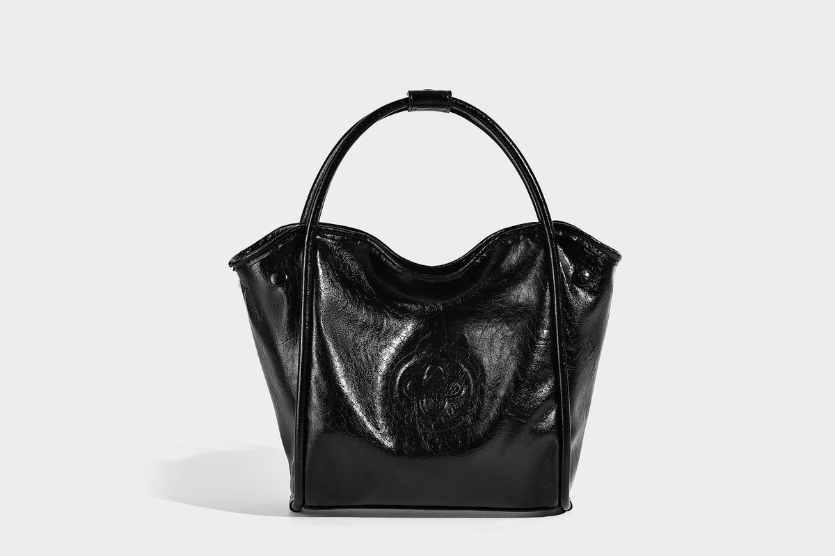 Glossy leather-look structured tote bag with rounded top handles, detachable shoulder strap, embossed front emblem, and side