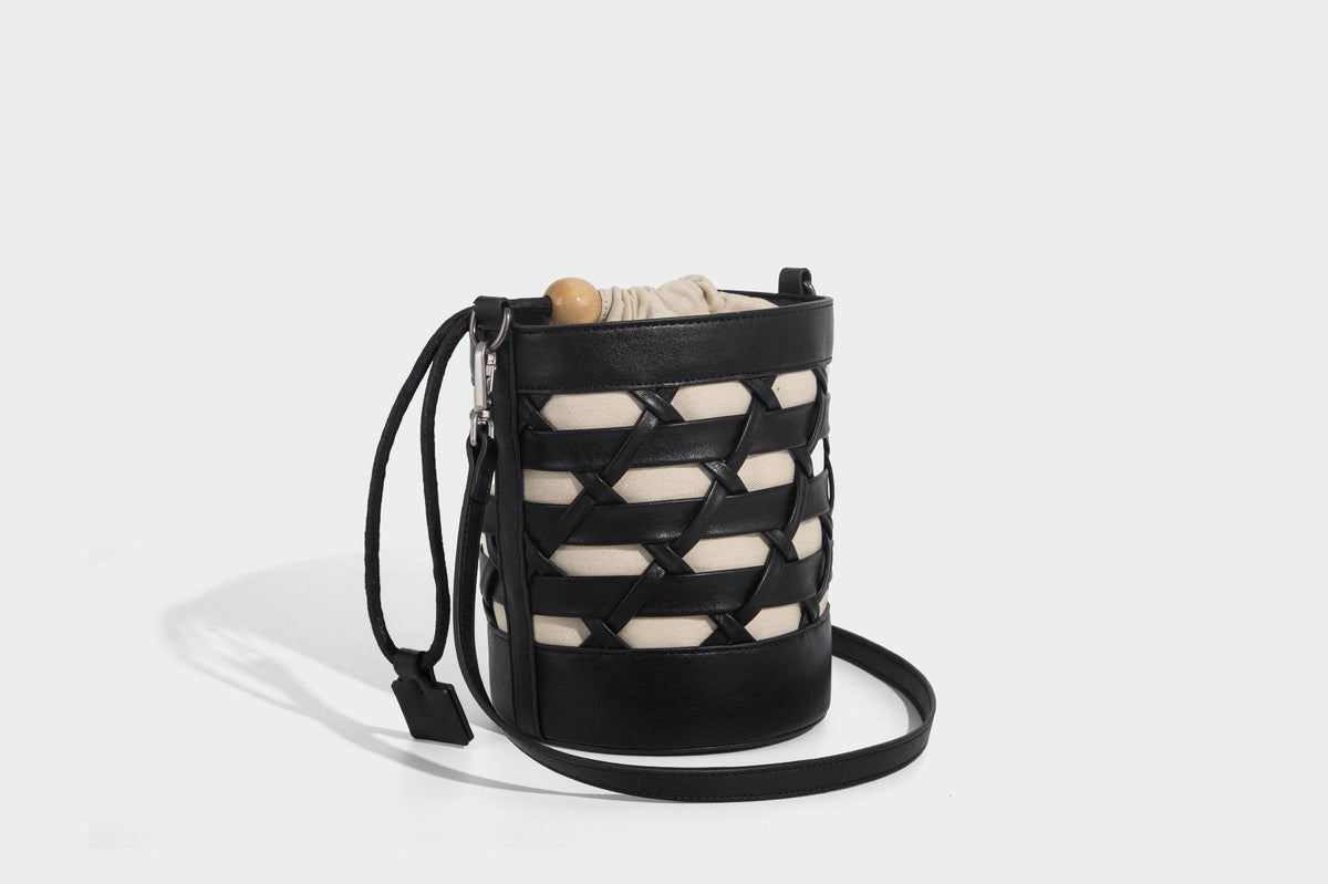 Small cylindrical woven lattice bucket bag with leather-look black trim, beige canvas body, wooden bead drawstring closure