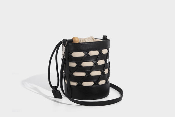 Small cylindrical woven lattice bucket bag with leather-look black trim, beige canvas body, wooden bead drawstring closure